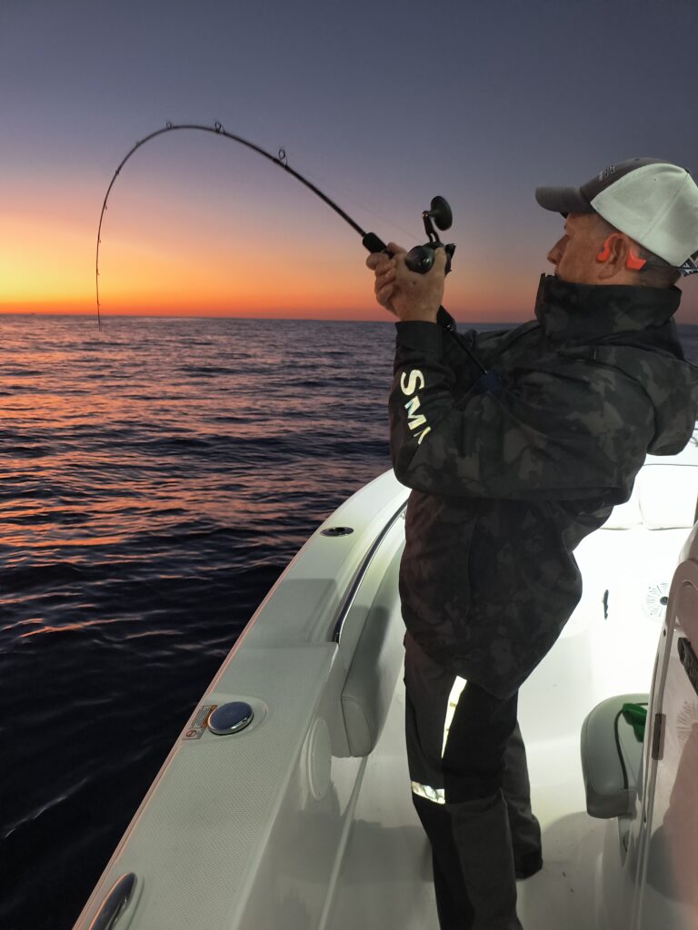 Angler fighting a fish on a bent rod during a Pensacola offshore jigging charter at sunset