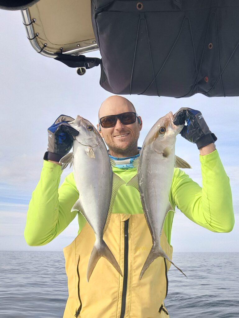 Angler holding two amberjack caught slow pitch jigging offshore from Pensacola